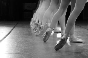A black and white photo of the legs of dancers, they are at a ballet lesson.