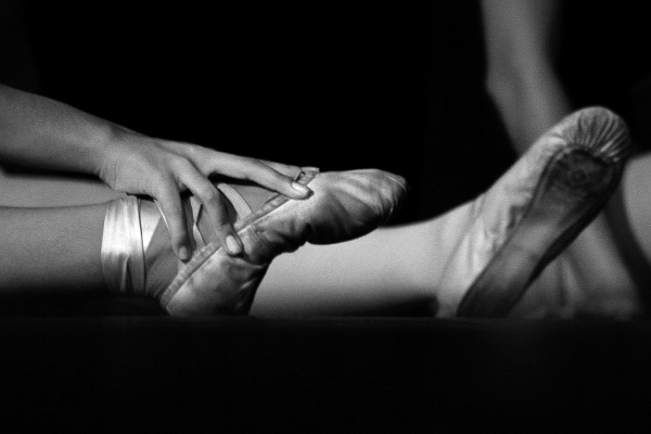 A black and white picture of someone steching out thier feet in ballet shoes.