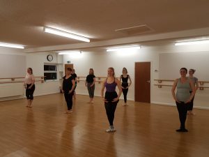 A group of young women stood in a starting position in an adult ballet class.